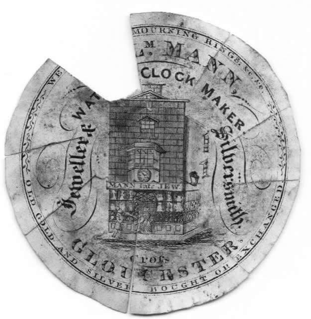 Engraved trade card for M. Mann, Clock Maker, Late Jew, Goldsmith, of Gloucester, with the inscription Old Gold and Silver Bought or Exchanged, surrounding an engraving of a clock-tower shop with figures on the street